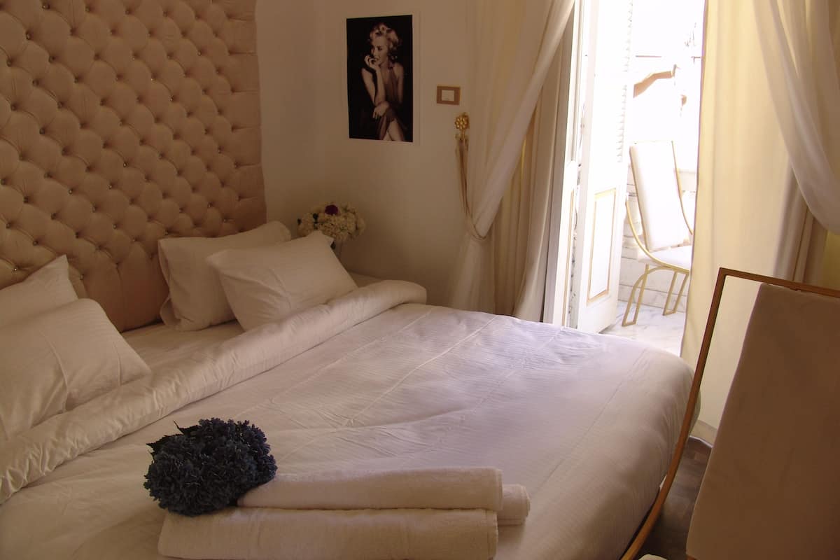 A bedroom with a tufted headboard, a bed with white linens, a decorative pillow, and a framed picture on the wall.