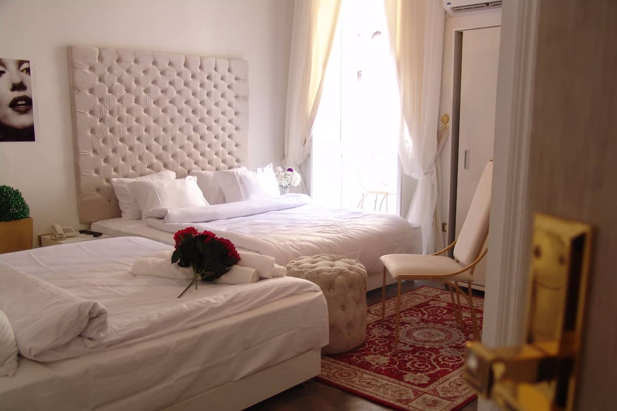 A hotel room with two beds, a red patterned rug, and a white chair.