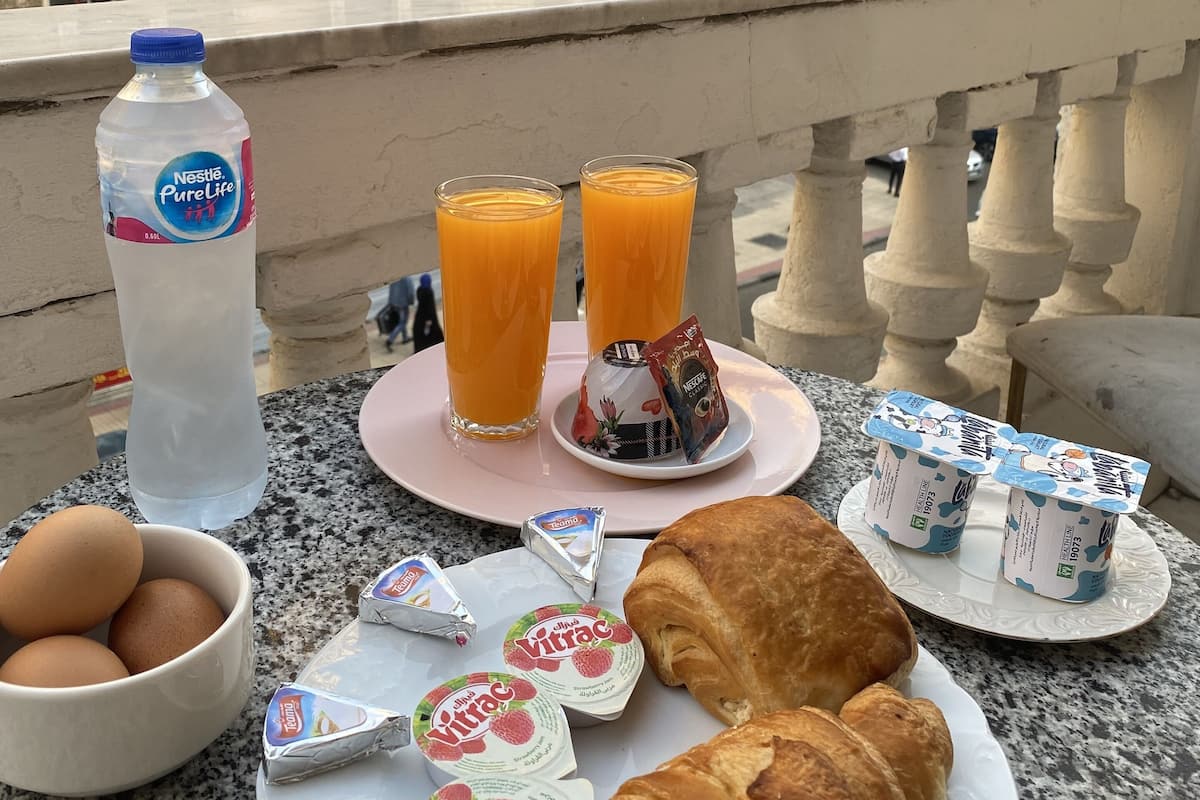 A breakfast setup with eggs, juice, yogurt, and croissants on a balcony with a cityscape view.