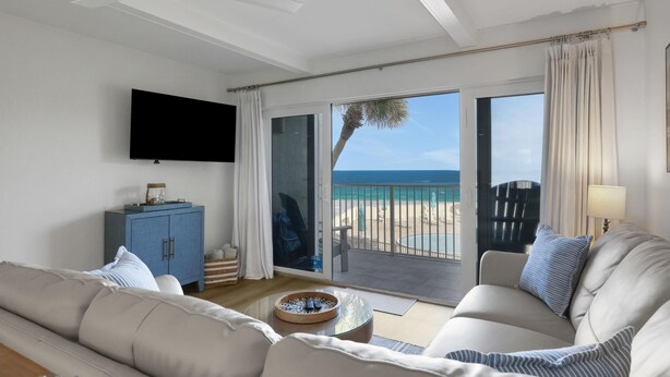 Una sala de estar con sofá, una mesa de centro, televisor y vista a la playa.