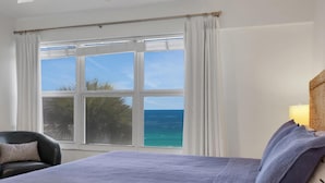 Una habitación de hotel con cama, una silla, un ventanal con vistas al océano y una lámpara.