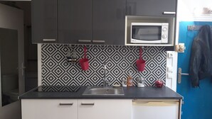 A modern kitchen with black cabinets, a white countertop, a microwave, and a sink. - Lovely studio in the heart of the historic center (Montpellier)