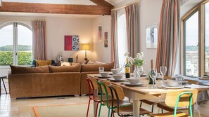 Een gezellige woonkamer met een bruine bank, een eettafel gedekt met borden, glazen en een fles, en uitzicht op groen buiten.