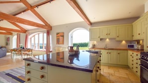 A spacious kitchen with a large island, wooden beams, and a view to the outdoors. - Oldbury Barn - sleeps 11 guests  in 4 bedrooms (Cheltenham)