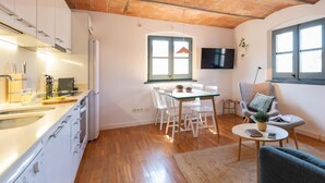 A modern kitchen with white cabinets, a dining area with a table and chairs, a TV mounted on the wall, and a cozy seating area with a sofa and a small table. - Bravissimo Raïms Penthouse, with 2 bedrooms (Girona)