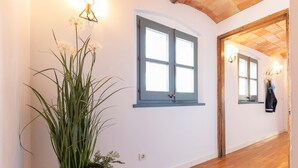 A hallway with wooden flooring, a potted plant, a blue-framed window, and a coat rack with a jacket. - Bravissimo Raïms Penthouse, with 2 bedrooms (Girona)