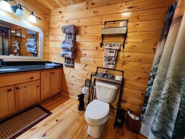 A wooden cabin bathroom with a sink, toilet, towel rack, and a small shelf with toiletries.