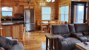 Ein gemütliches Blockhaus-Interieur mit Holzausstattung, einem Essbereich, einem Wohnzimmer mit Sofa und einer Küche mit Kühlschrank.