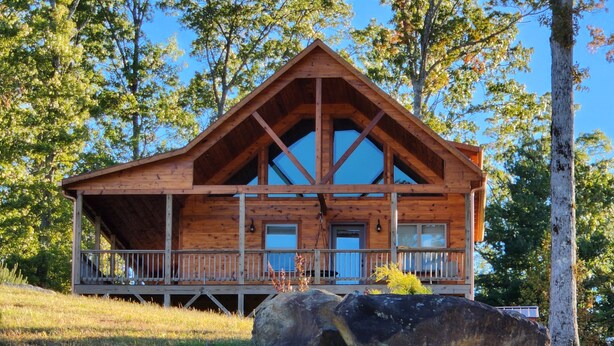 Eine Holzhütte mit Veranda, großen Fenstern und einem Steinfundament.