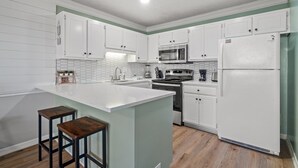 A kitchen with white cabinets, a central island with stools, a microwave, stove, and refrigerator.