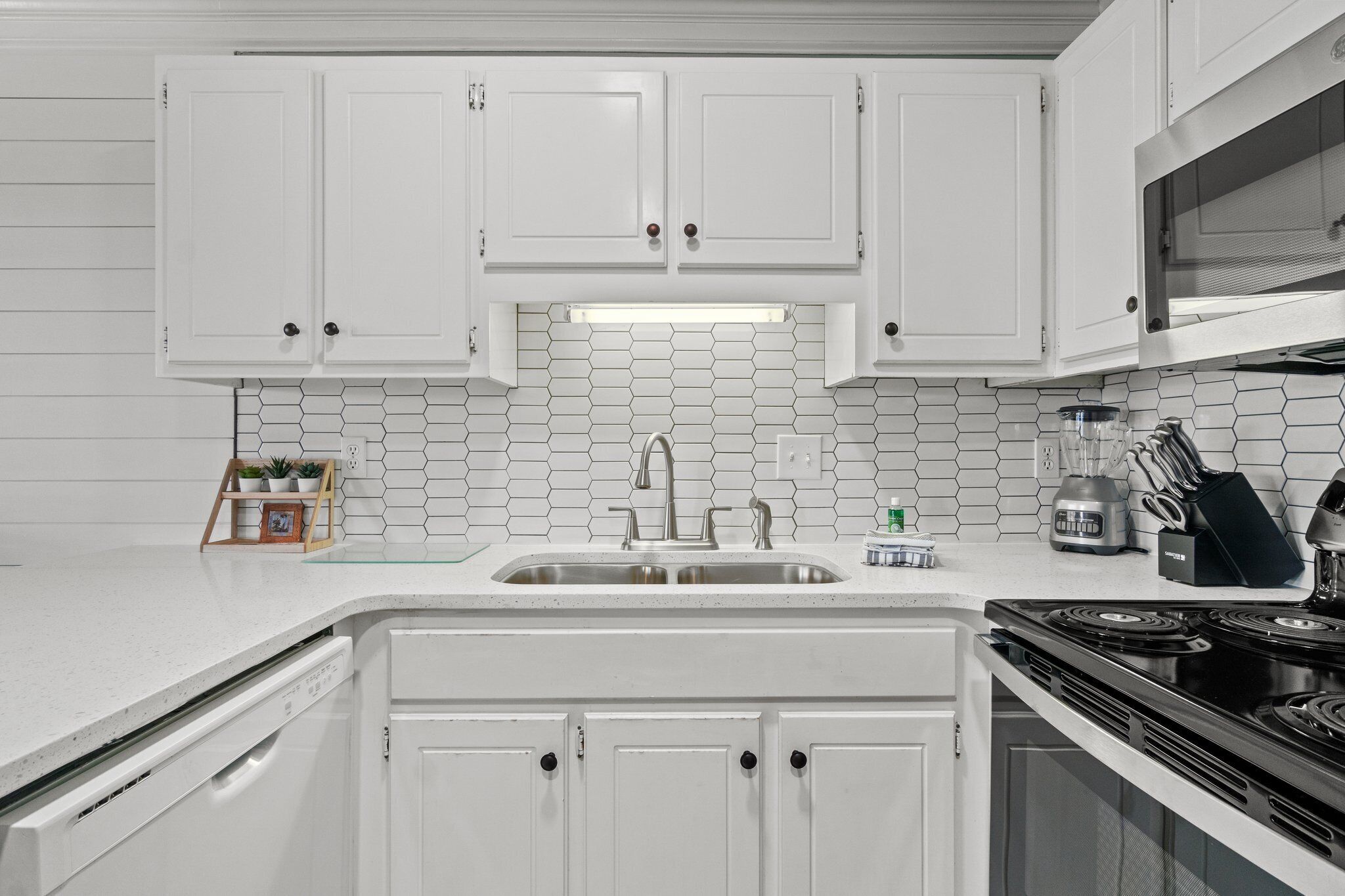 A kitchen with white cabinets, a stainless steel sink, a microwave, and a stove.