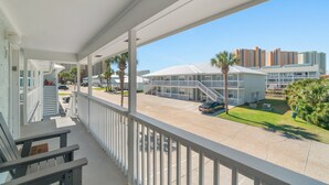 A balcony with a view of a parking lot, a building with a white roof, and palm trees.