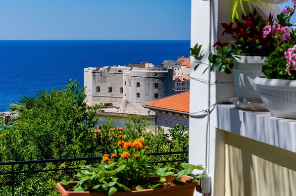 A balcony with potted plants and a view of a historic stone building by the sea. - Room Mimi - Double Room with patio and sea view (Dubrovnik)