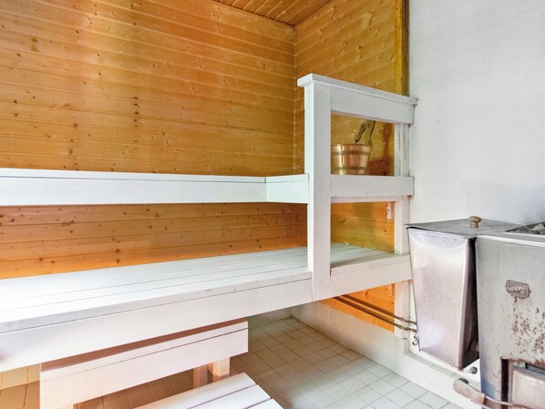 A wooden cabin interior with a bunk bed, a small kitchen area with a stove, and a window with a metal bucket.