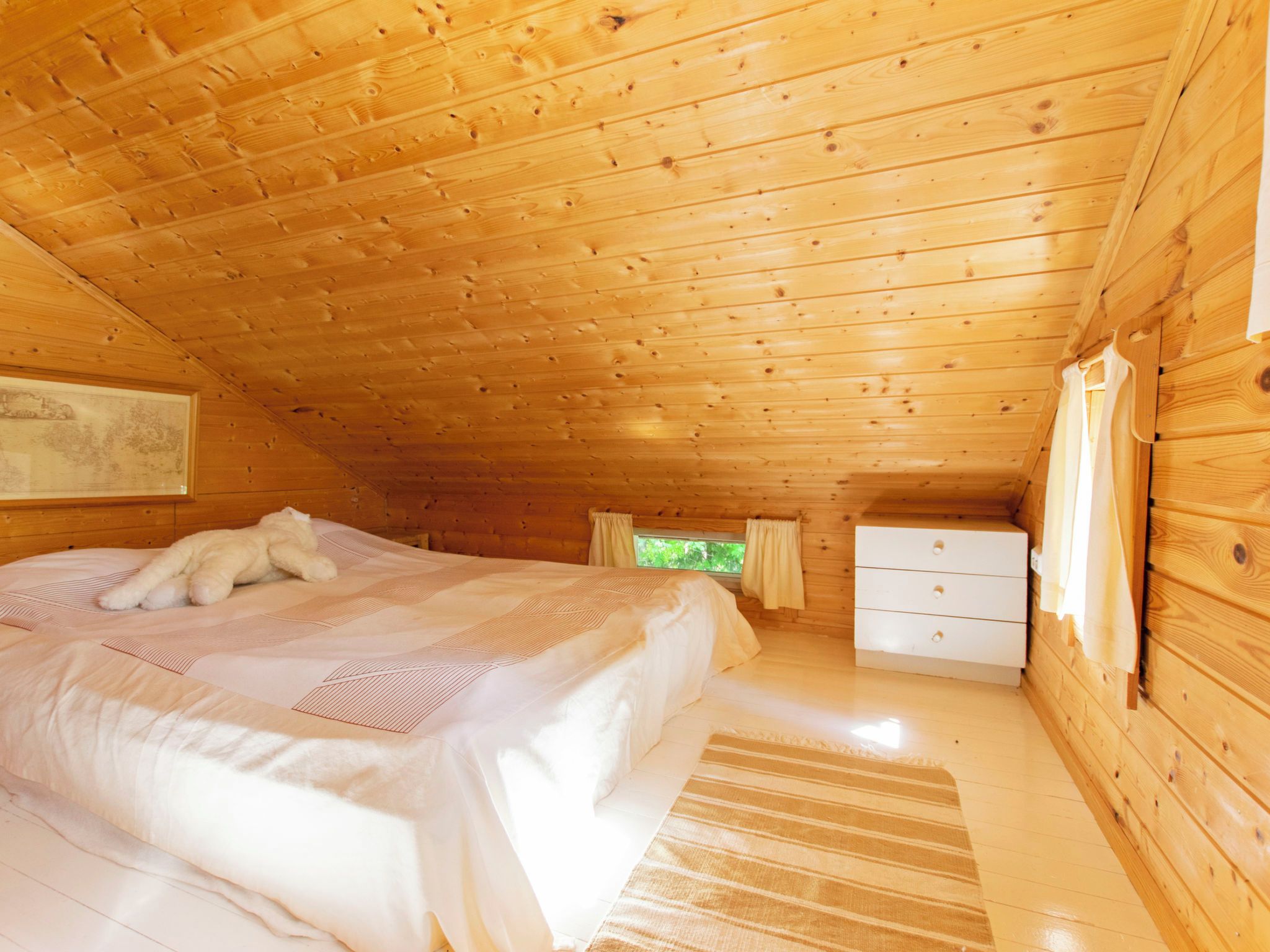 Ein gemütliches Schlafzimmer einer Holzhütte mit einem Bett, einer Kommode und einem Fenster.