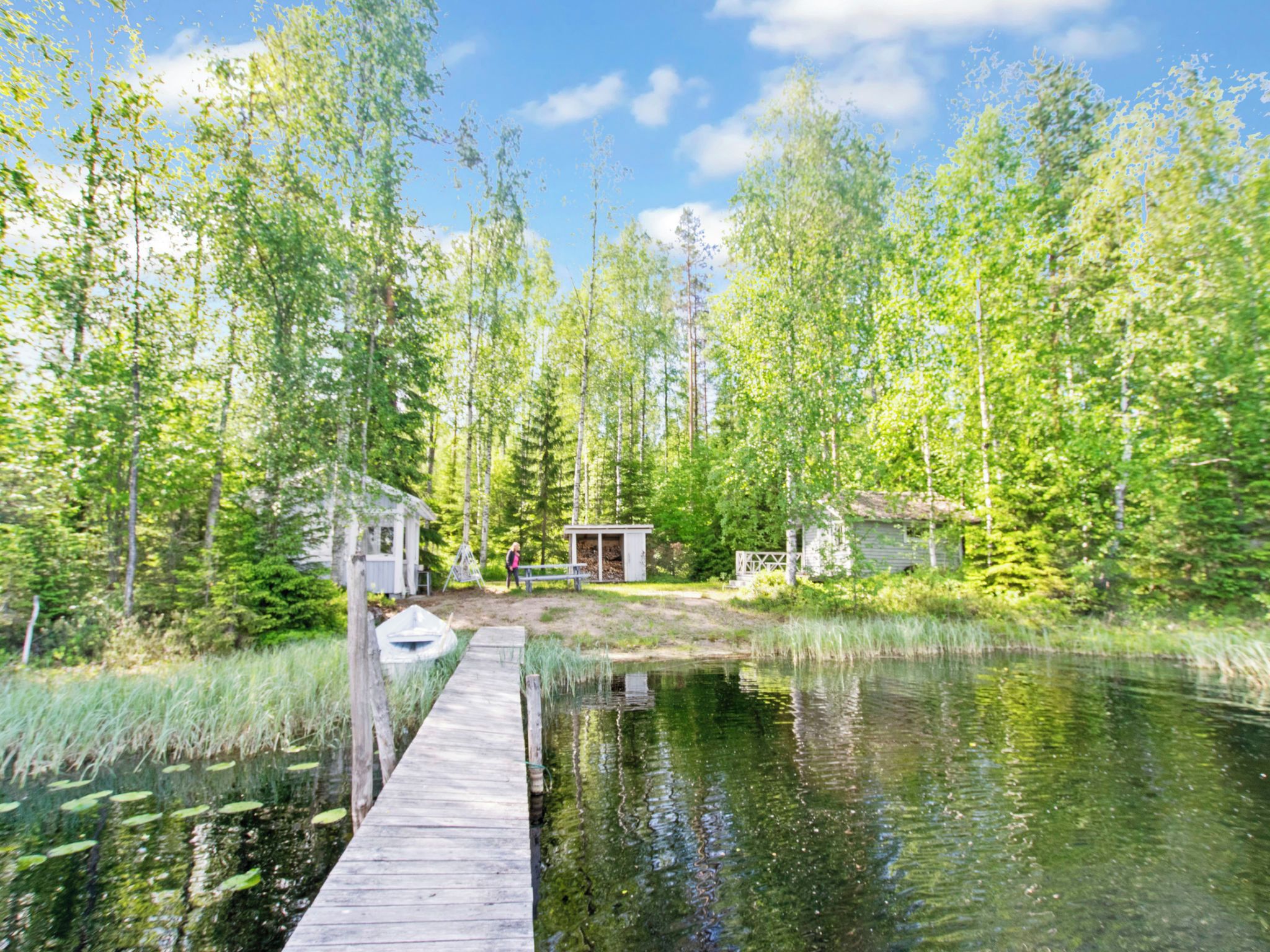 Eine Holzstege führt zu einer kleinen Holzhütte, umgeben von Wald und einem Teich.