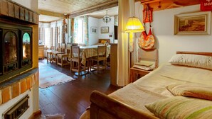 A cozy room with a wooden ceiling, a fireplace, a dining area with a table and chairs, and a bed with pillows. - Piennarpää by Interhome (Saarijärvi)