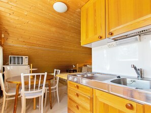 A compact kitchen with wooden cabinets, a stainless steel sink, and a microwave. - Piennarpää by Interhome (Saarijärvi)
