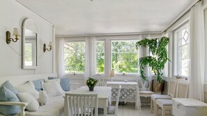 A bright, white room with a sofa, a dining table, and chairs. There are windows with curtains, a mirror, and a potted plant. - Piennarpää by Interhome (Saarijärvi)