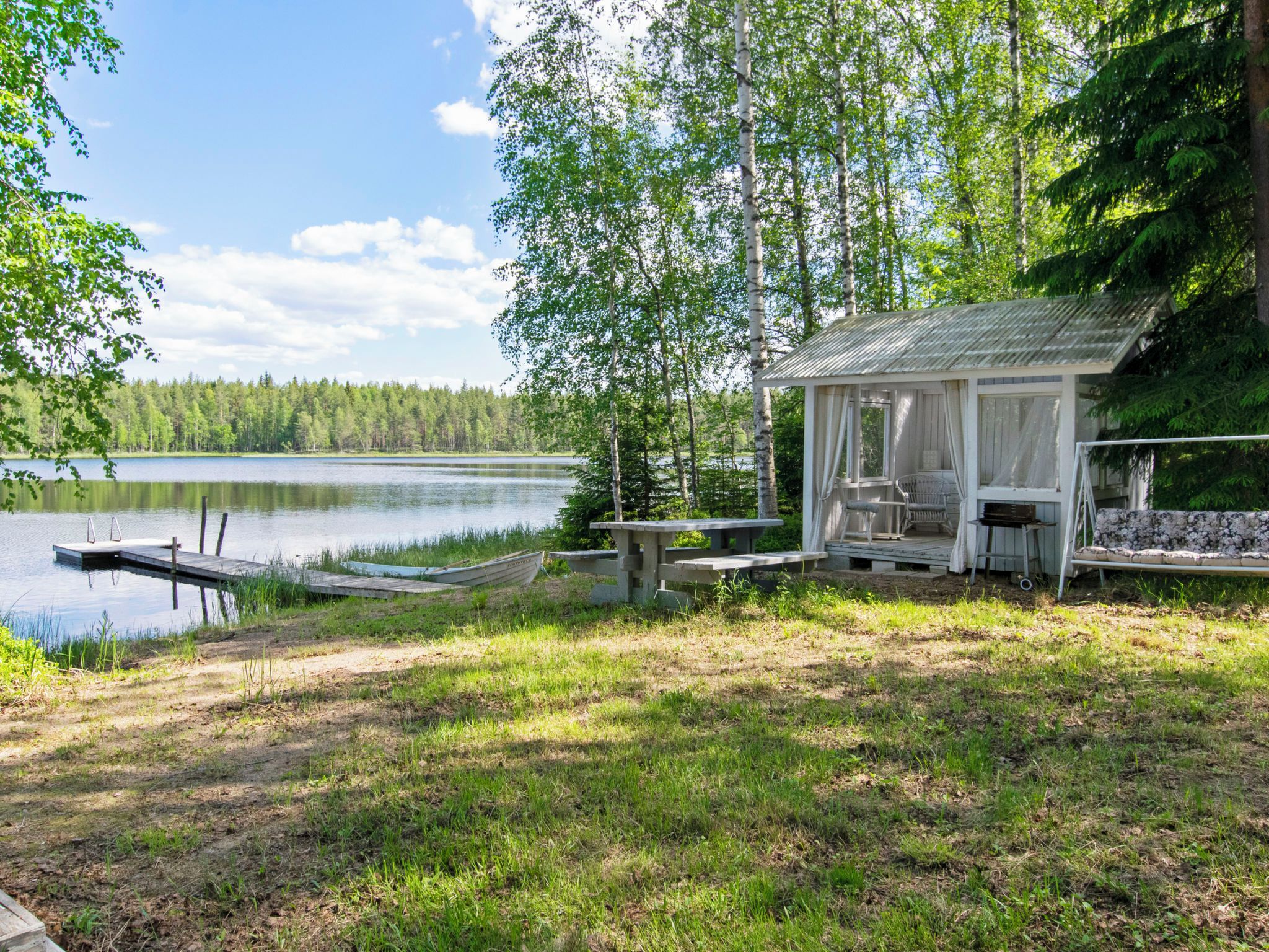 A lakeside cabin with a dock, outdoor seating, and a view of the lake and forest.