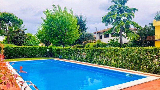 Ein rechteckiger Swimmingpool mit Metallleiter an einer Seite, umgeben von einer gefliesten Poolterrasse.