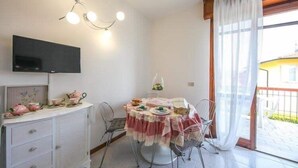 Ein Essbereich mit rundem Tisch, Stühlen, einem an der Wand montierten Fernseher und einem Fenster mit Vorhängen.