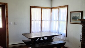 Um quarto com uma mesa de madeira e bancos, um sofá de couro, um tapete estampado e um quadro na parede.