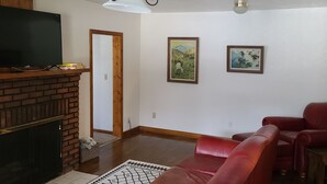 Uma sala de estar com lareira, sofá de couro vermelho e duas imagens emolduradas na parede.