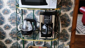 Uma área de cozinha com uma estante de metal verde que acomoda um micro-ondas, uma cafeteira e uma cesta com um pacote de café.