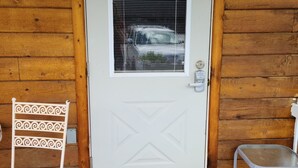 Uma porta branca com uma janela, uma cadeira branca com encosto decorativo e uma pequena mesa ao lado da porta.
