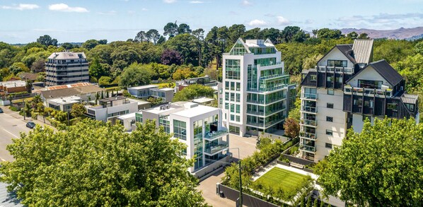 A modern residential area with contemporary architecture, including multi-story buildings with large windows and balconies, surrounded by lush greenery and a clear sky. - The Carlton Apartments (Christchurch)