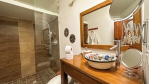 Une salle de bain avec une douche en verre, un meuble-lavabo en bois, un lavabo agrémenté d’un récipient décoré de motifs floraux et un miroir.