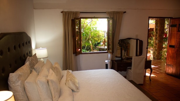 Une chambre à coucher avec un lit, un bureau, une chaise, une lampe et une fenêtre avec des rideaux.