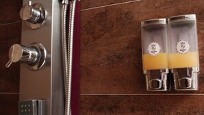 Un espace douche doté de robinetterie chromée et de deux distributeurs en verre contenant un liquide jaune.