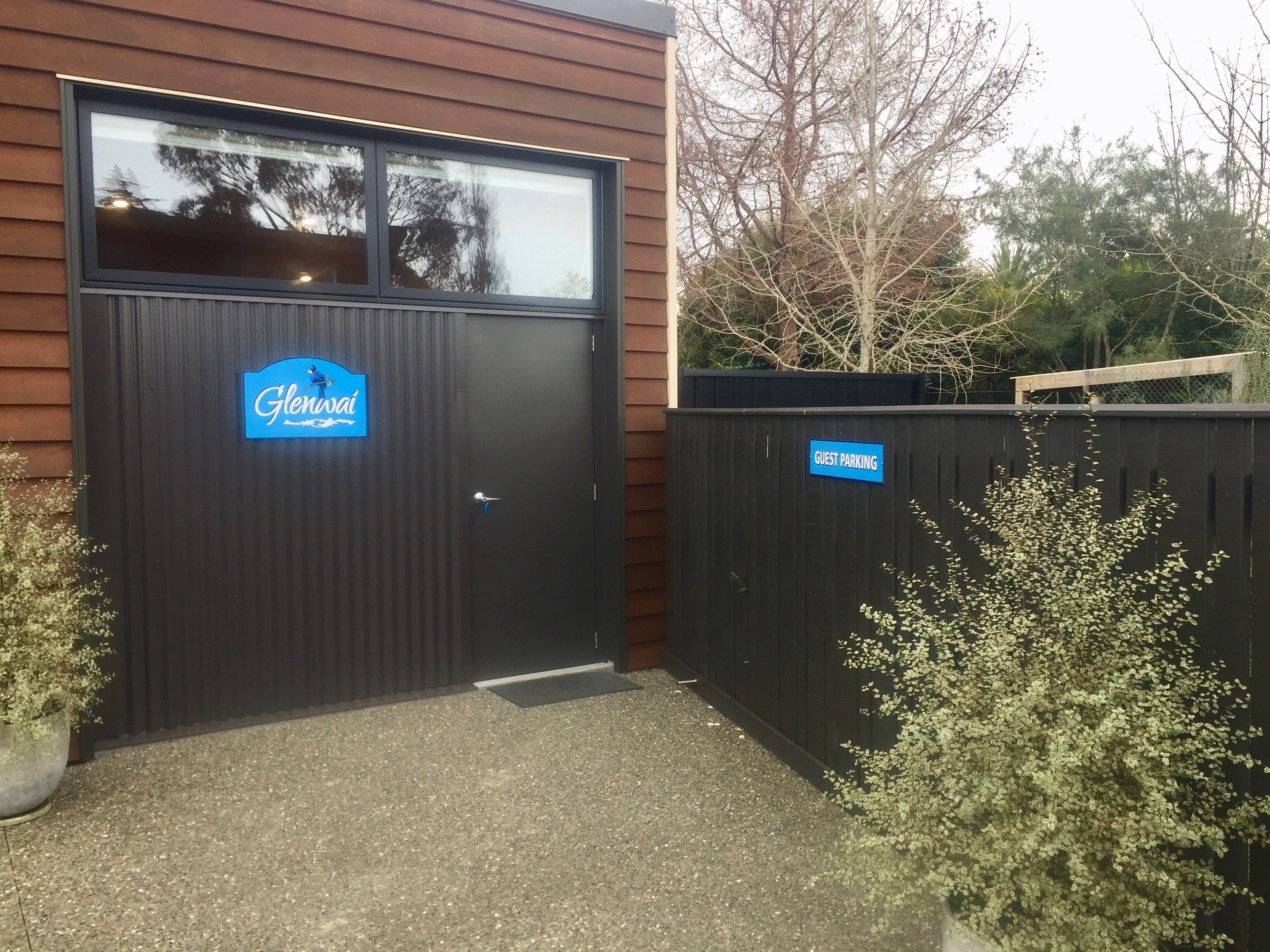 Une porte de garage noire avec une enseigne « Glendale » et une autre indiquant « Stationnement réservé aux invités » sur une clôture.