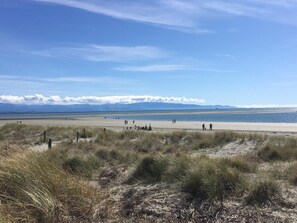 Uma praia extensa com pessoas caminhando, céu claro e montanhas ao longe.