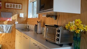 A modern kitchen with wooden walls, a built-in microwave, a toaster, and a vase with flowers on the counter. - Self contained unit. By the beach and golf course  only 2.2 kms to town centre (Motueka)