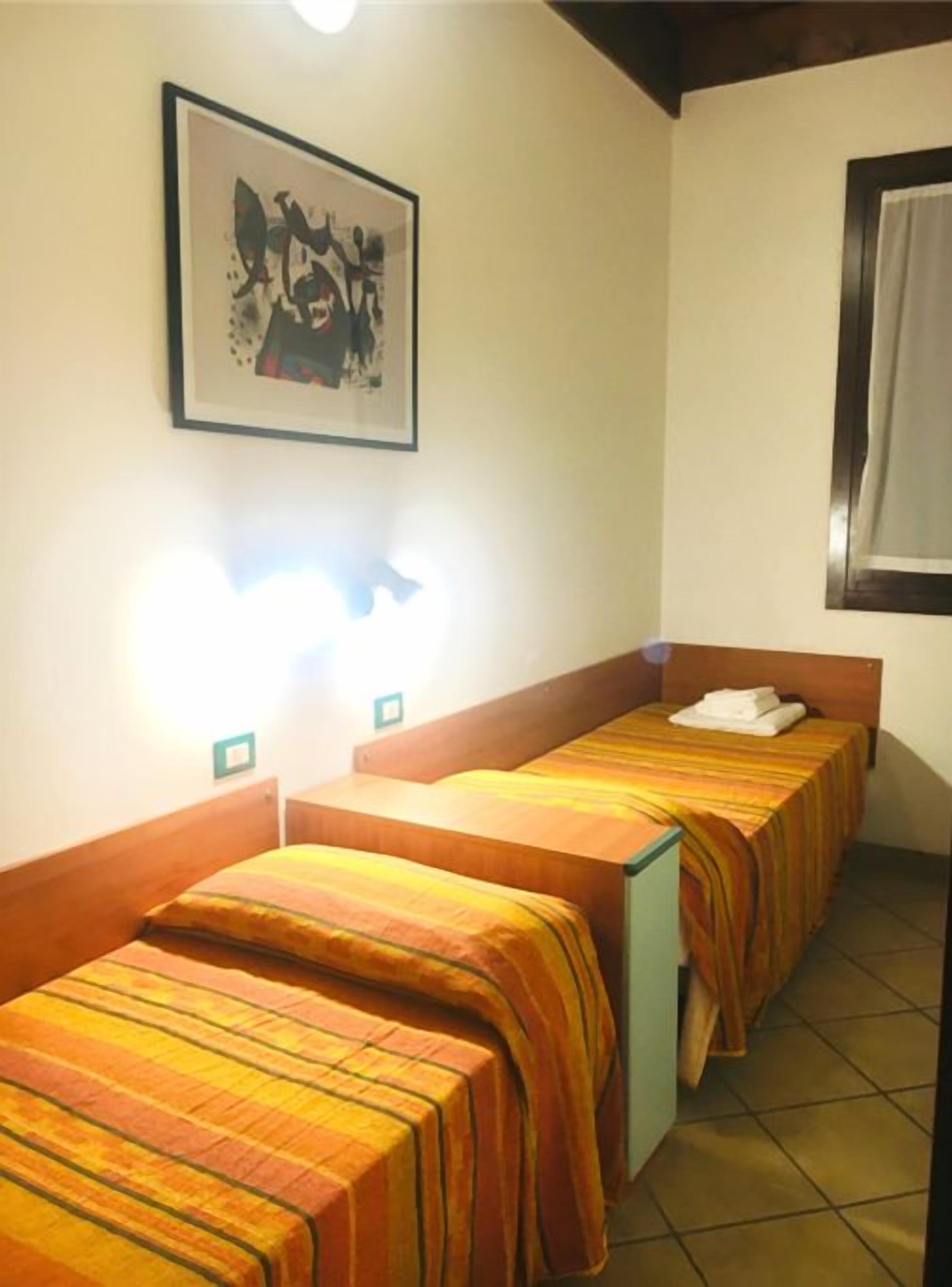 Ein Hotelzimmer mit zwei Einzelbetten, einem gerahmten Bild an der Wand und einem Fenster mit Vorhang.