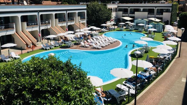 A pool area with multiple lounge chairs and umbrellas, surrounded by buildings with balconies. - Alba 4 pers. - One Bedroom Resort, Sleeps 4 (Lido di Spina)