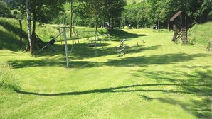 Een groen park met speeltoestellen, bomen en een klein houten gebouw.