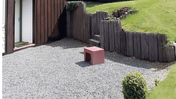 Een huis met een schuin dak, een klein portaaltje en een oprit met grind.