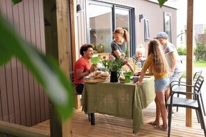 Un área de comedor al aire libre con techo, una mesa lista para una comida, rodeada de paredes de madera y un ventanal.