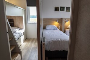 Un dormitorio pequeño con una cama litera y una cama individual, una ventana con vistas, y un estante.