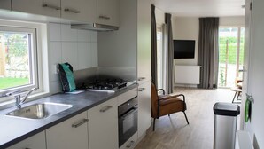 Une cuisine moderne avec des armoires blanches, un évier en acier inoxydable et une cuisinière à gaz. On y trouve une chaise et un téléviseur fixé au mur.