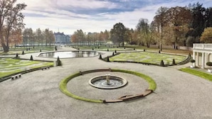 Un jardín formal con una fuente central, senderos simétricos y céspedes cuidados.