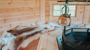 L’intérieur d’un chalet rustique en bois, avec un plancher recouvert de peaux, une bouilloire en métal suspendue au plafond et un poêle en métal.