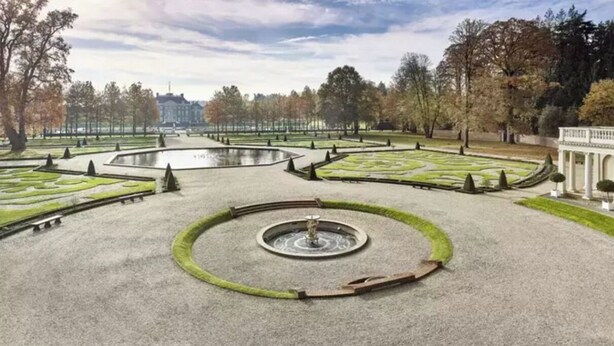 Un jardin à la française, avec une fontaine centrale, des allées disposées de manière symétrique et des pelouses parfaitement entretenues.