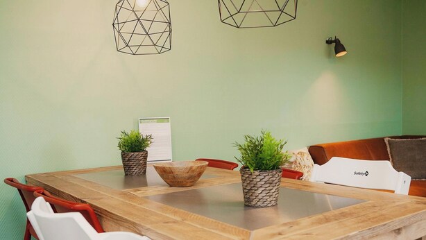 Una mesa de madera para comer con dos plantas en macetas, un cuenco de madera y una silla blanca.