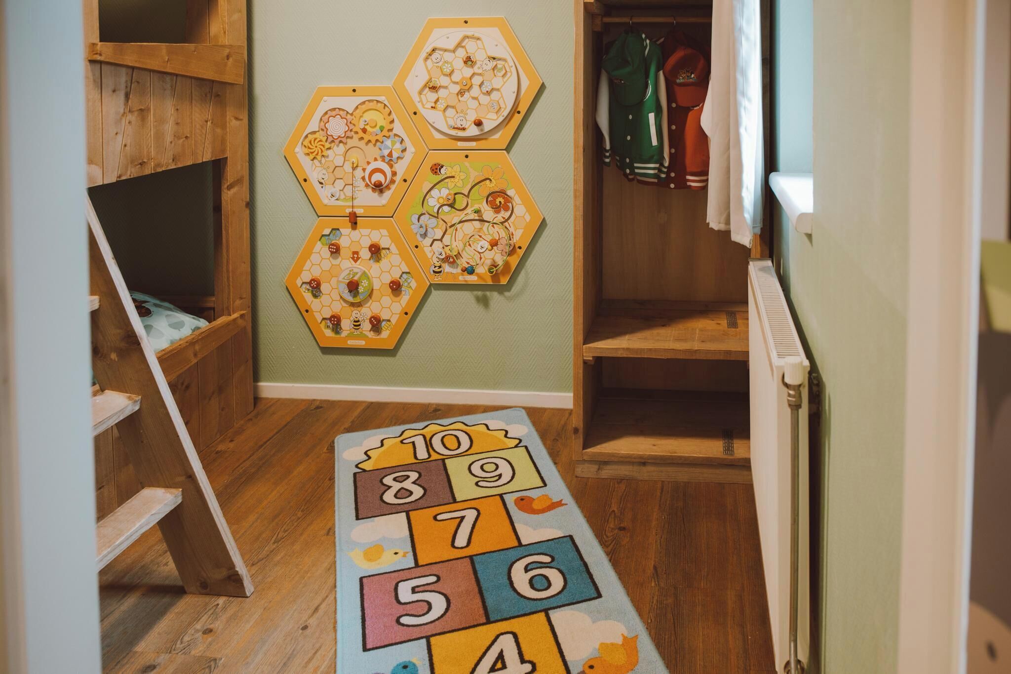 Un espace de jeux pour enfants avec une échelle en bois, un tapis de jeu orné de chiffres et un mur décoré de motifs hexagonaux.