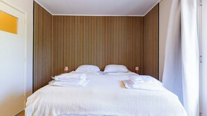A neatly made bed with white linens and towels, a wooden slatted headboard, and a white ceiling.